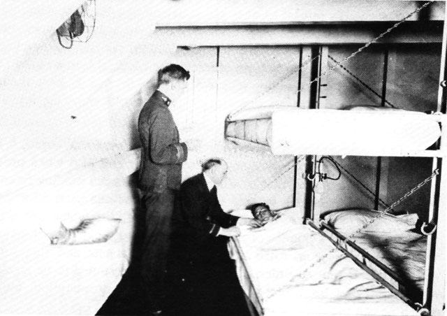 Medical Officer and Chaplain woith a patient in sickbay of USS RELIEF, circa 1920