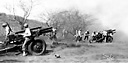 A BATTERY OF 105-MM. HOWITZERS M2A1 firing during maneuvers (top); 
ordnance men repairing small arms (bottom). Two men are holding .45-caliber
automatic pistols M1911; in the vice on the table is a .30-caliber Browning 
automatic rifle M1918A2; on the table are two .30-caliber rifles M1.