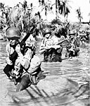 FIRST-WAVE TROOPS, armed with M1 rifles, wade waist deep through a stream en route to San Fabian