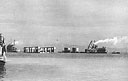 A tug (left) arrives at Amsterdam Island, Dutch New Guinea, towing a floating drydock, a 'double-bubble' gasoline barge, a crane barge, and a radar repair barge