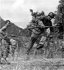 INFANTRYMAN CLIMBING OVER A BARBED WIRE FENCE during training at the Unit Jungle Training Center