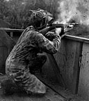 SOLDIER WEARING A CAMOUFLAGE SUIT fires a .45-caliber Thompson submachine gun