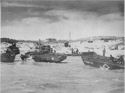 U.S. COAST GUARD-MANNED LANDING BARGES AND HEAVILY LOADED AMPHIBIOUS TRUCKS RUSH SUPPLIES TO A SICILIAN SHORE