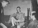 TWO COAST GUARDSMEN HOLD A DISCUSSION WITH A WOUNDED PARATROOPER