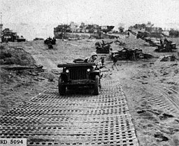 Figure 8.--Use of pierced steel plank to form beach roadway. Some such material will usually be needed to providxe sufficient bearing surface for vehicles. (Marines at Iwo Jima.)