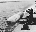 A Mark XIII torpedo slides from its launching rack, propellers spinning and exhaust gases escaping from its tail